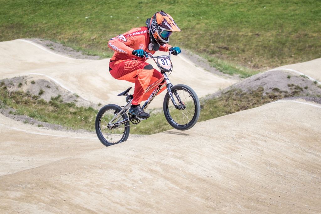BMX-renner met startnummer 31 landt na een schans op een Nederlandse BMX-baan met steile bochten en heuvels