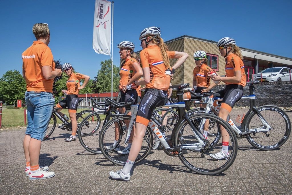 Junioren vrouwen in KNWU-wielershirt wachten met hun fietsen tijdens de verkenning van het NK-parcours