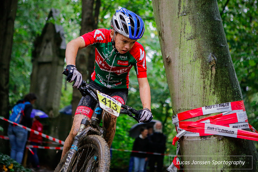 Jonge mountainbiker met rugnummer 413 stuurt door een modderig bospad tijdens het natte NK MTB voor de jeugd
